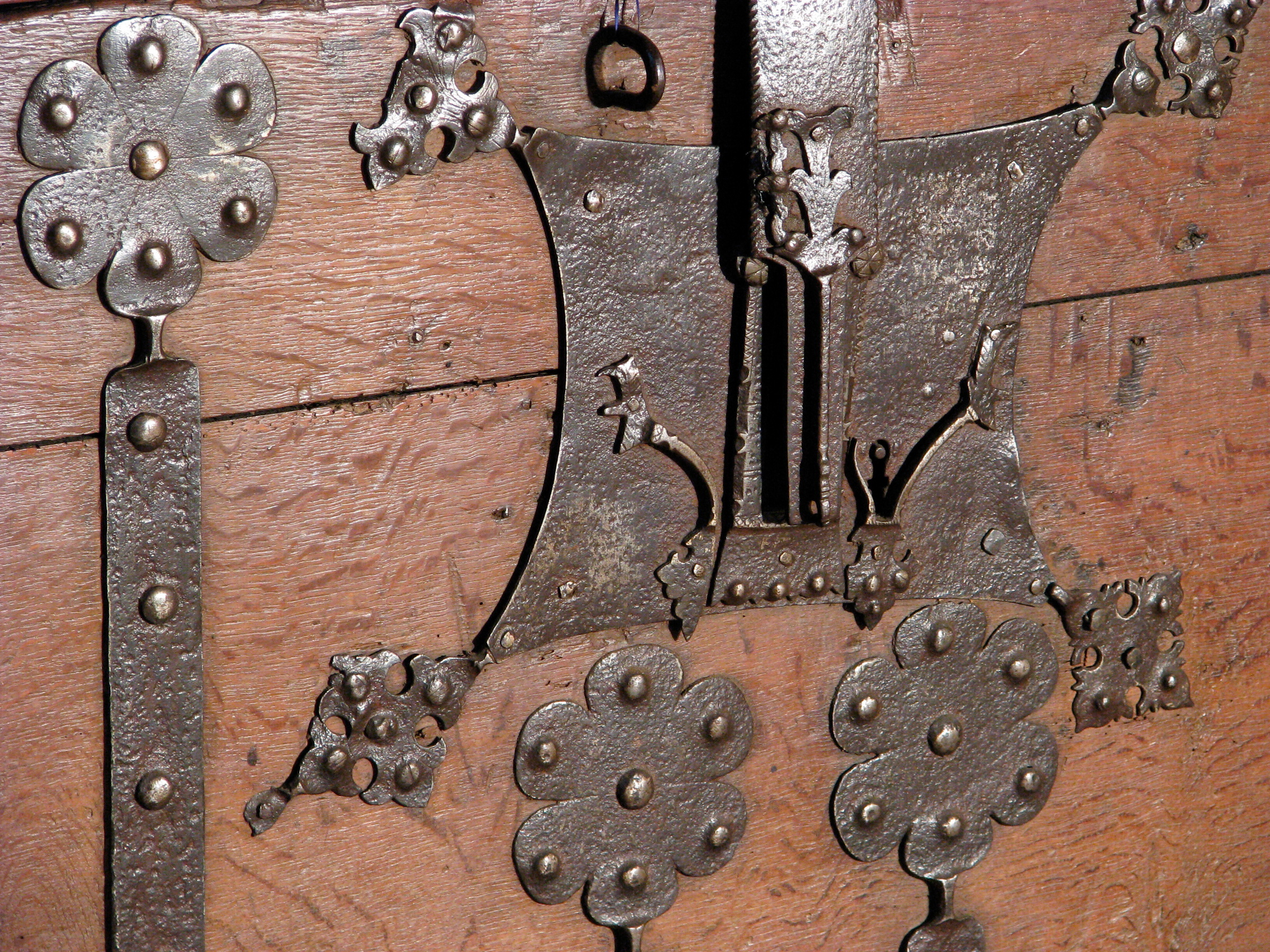 Ornate, antique metal lock and decorative hinges mounted on a wooden surface.
