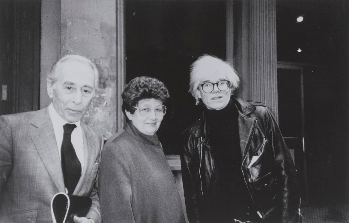 Three people pose together for a black and white photo, two in suits and one in a leather jacket.