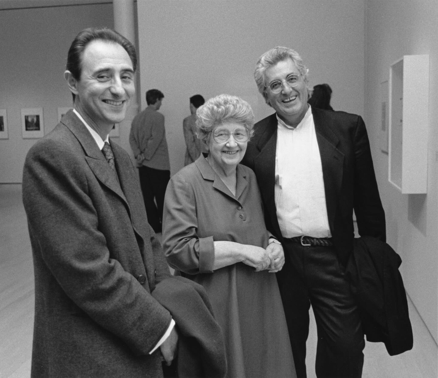 Three people are smiling and posing together in a gallery or museum space.
