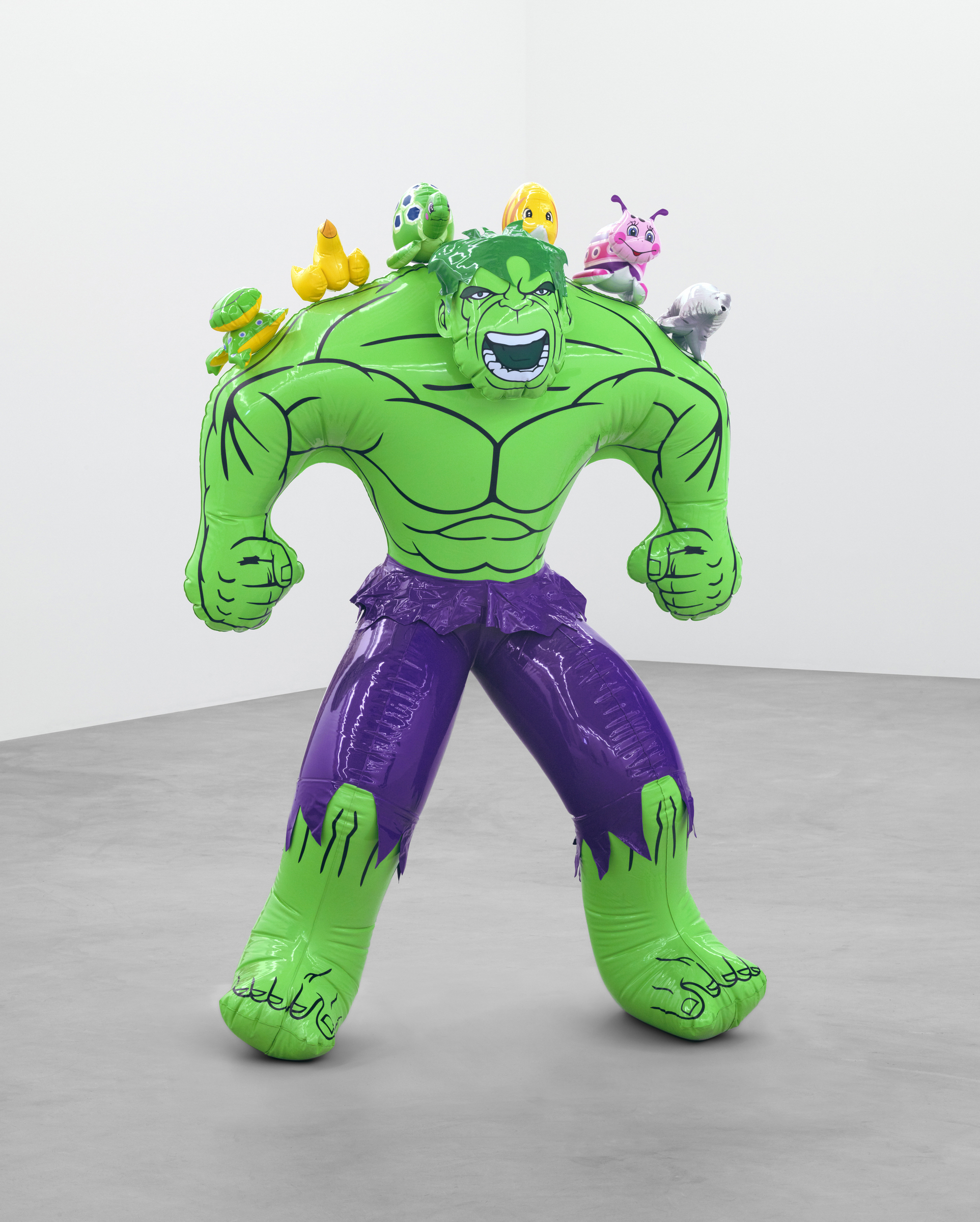 An inflatable Hulk figure with toys on its shoulders stands in a plain, empty room.
