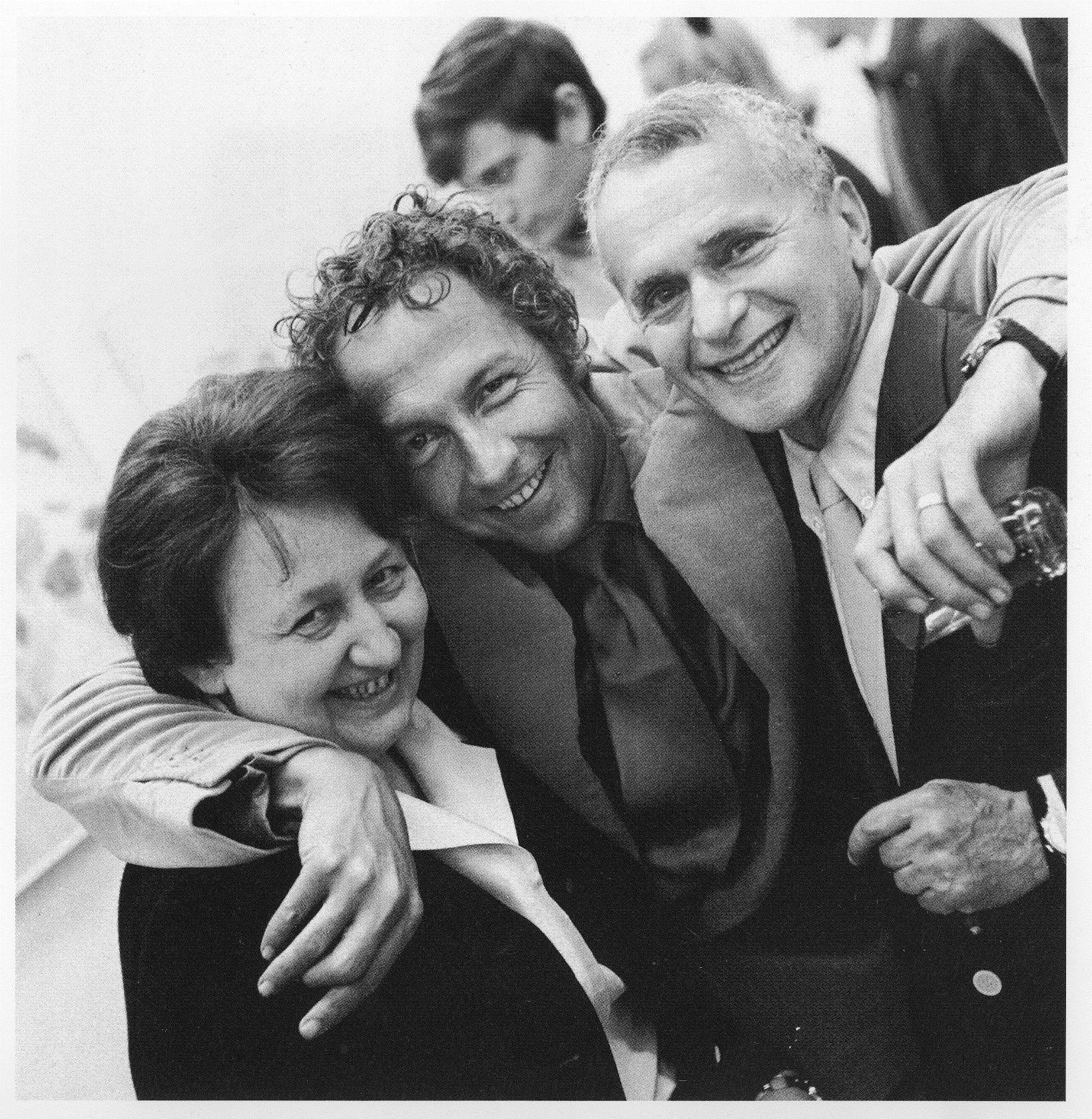 Three people are smiling and posing closely together at what appears to be a social event.