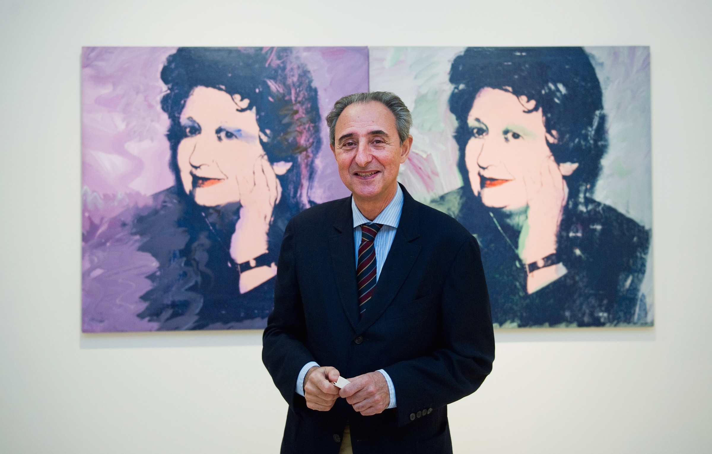 A man in a suit stands in front of two colorful pop art portraits of a woman on the wall.