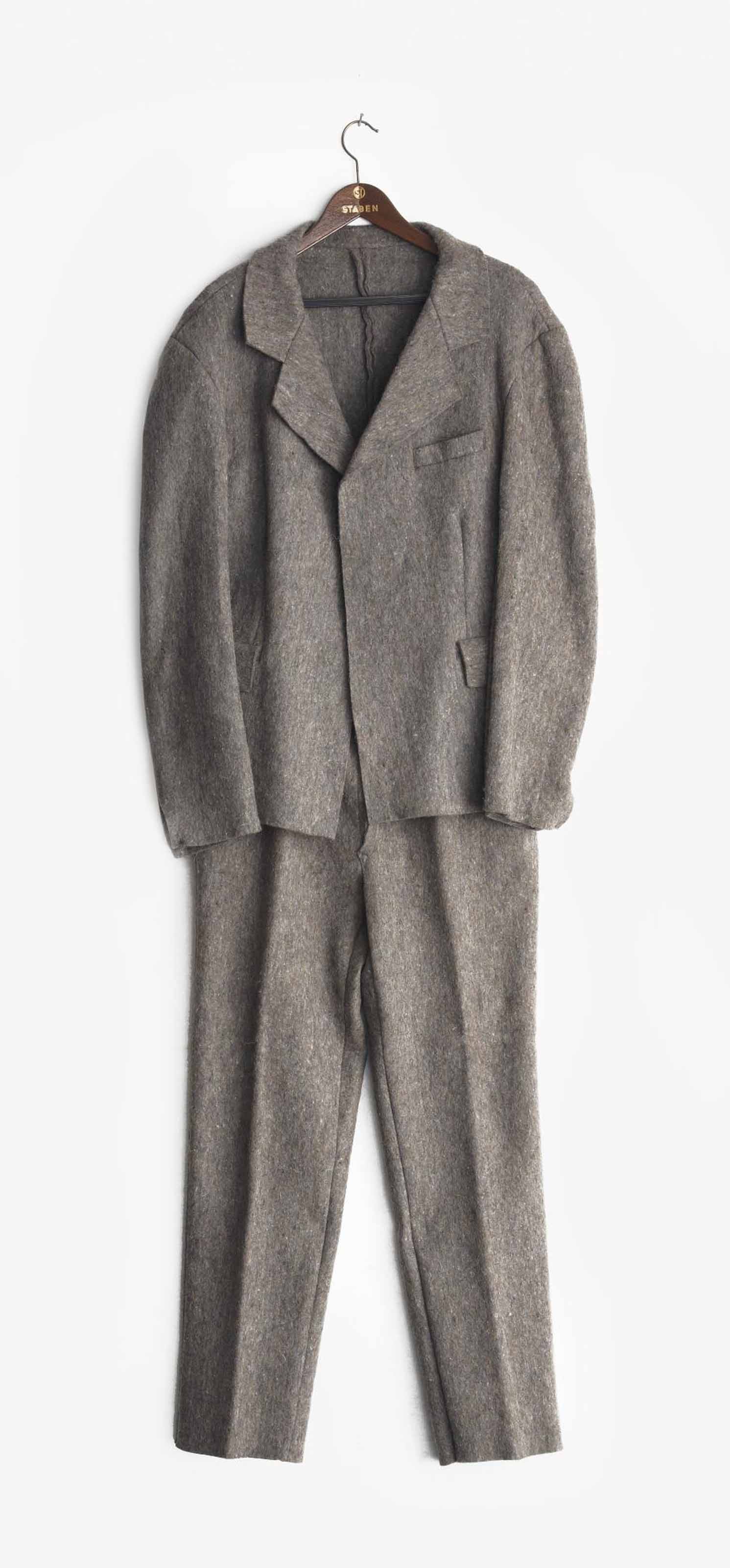 A gray woolen suit with a jacket and trousers is hanging on a wooden hanger.