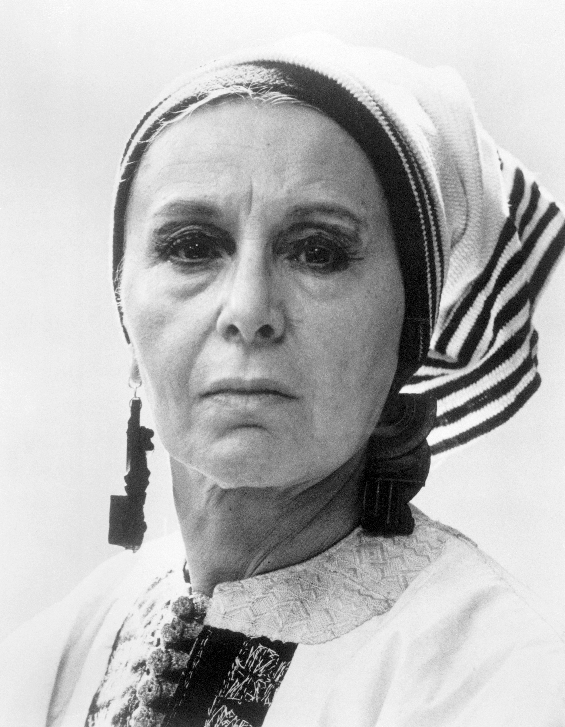 A woman wearing traditional clothing and a striped headscarf looks directly at the camera.