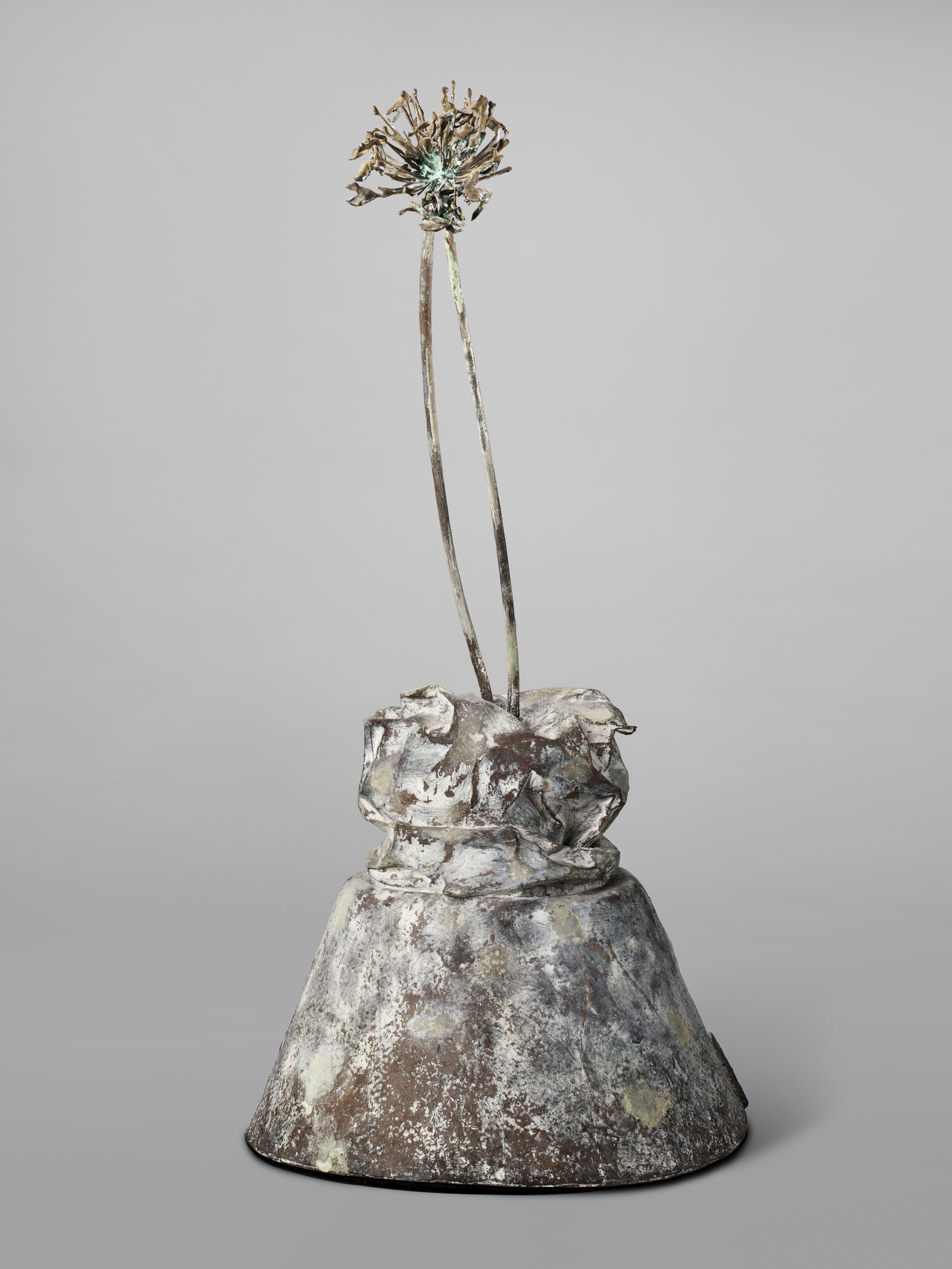 A metallic sculpture of a wilted flower with two stems emerges from a roughly textured base.