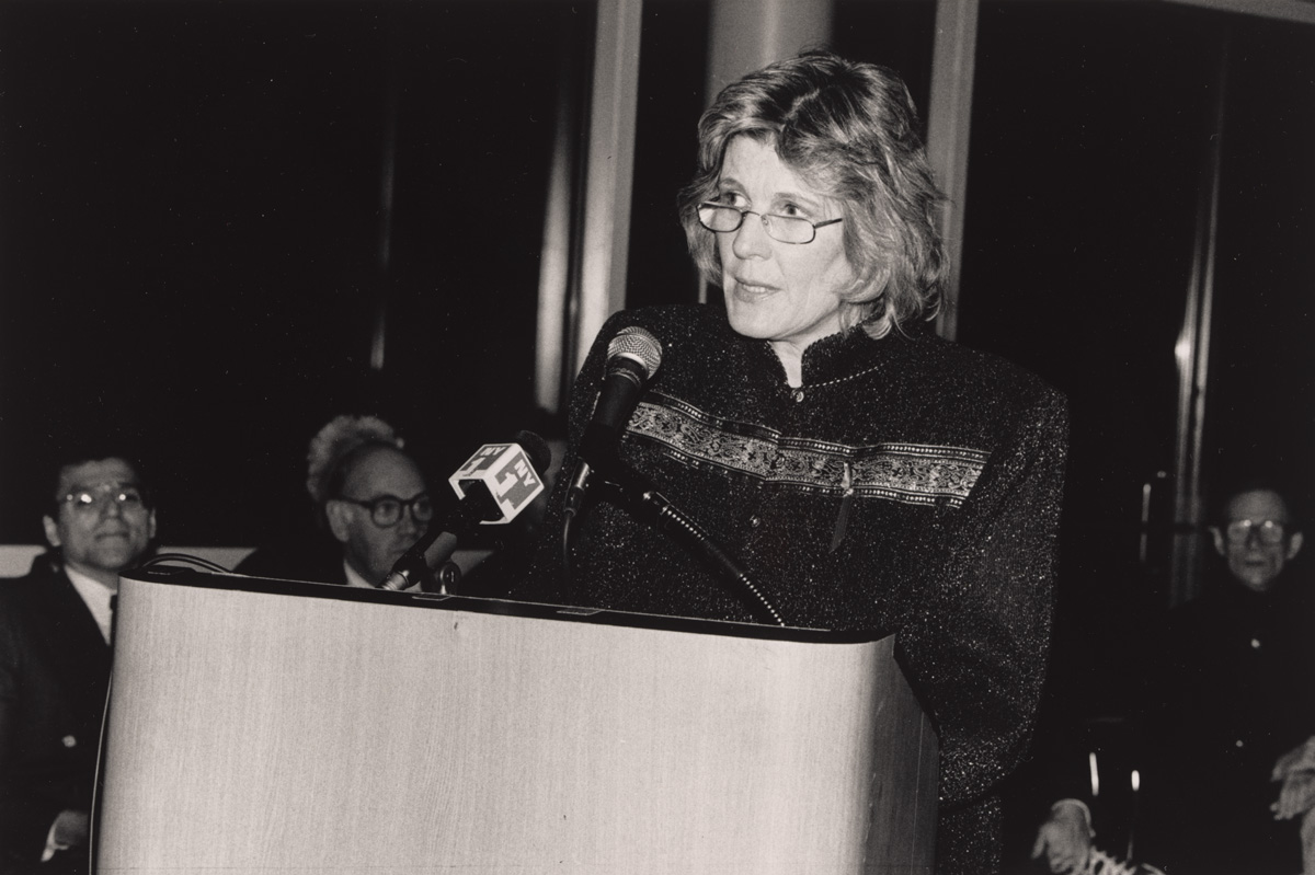 A woman is speaking at a podium with a microphone in a formal setting.