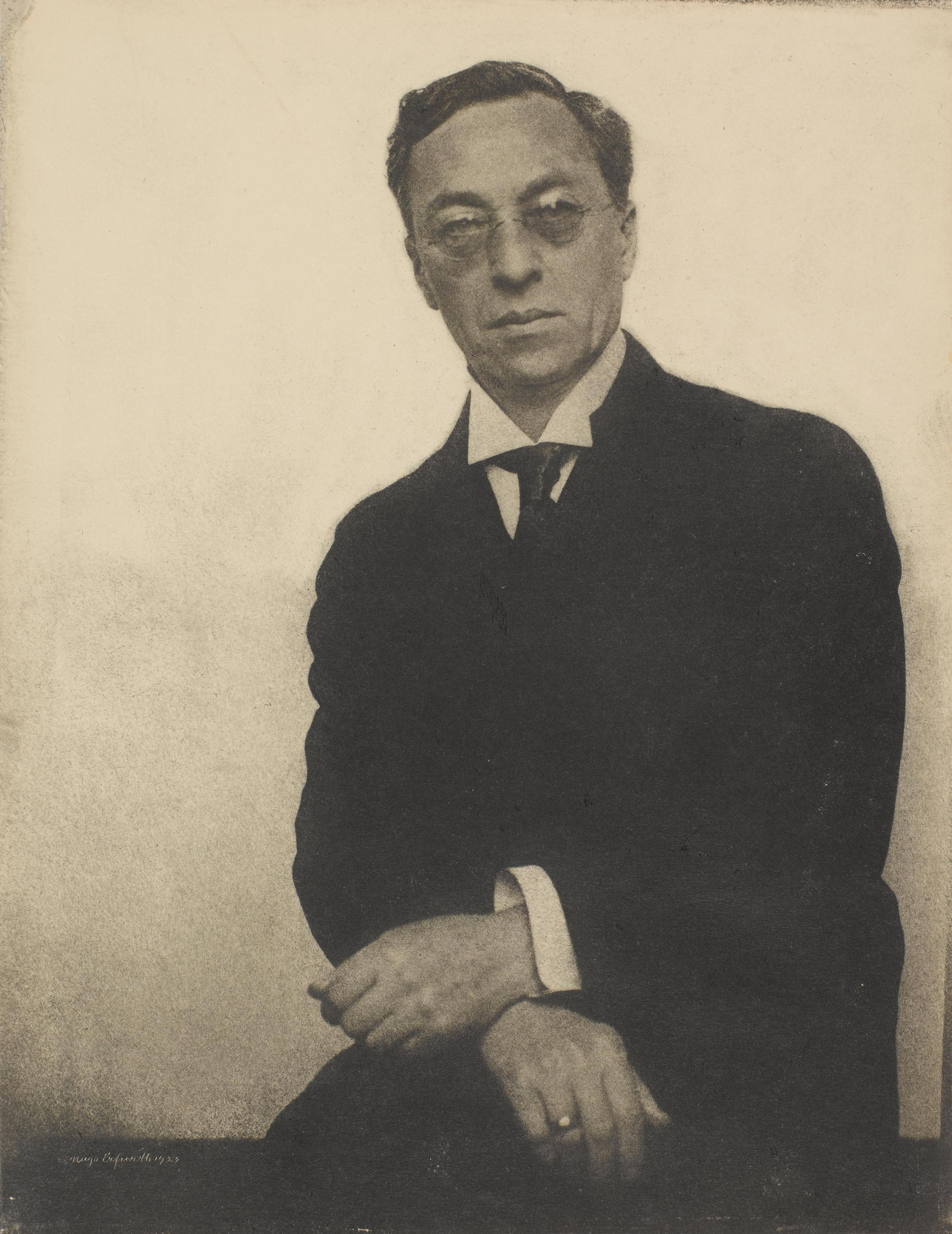 A man in a suit and glasses poses formally against a plain background in a vintage photograph.
