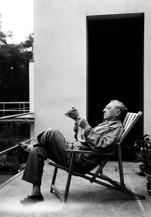 An elderly man sits in a deck chair outside, reading a newspaper and relaxing.