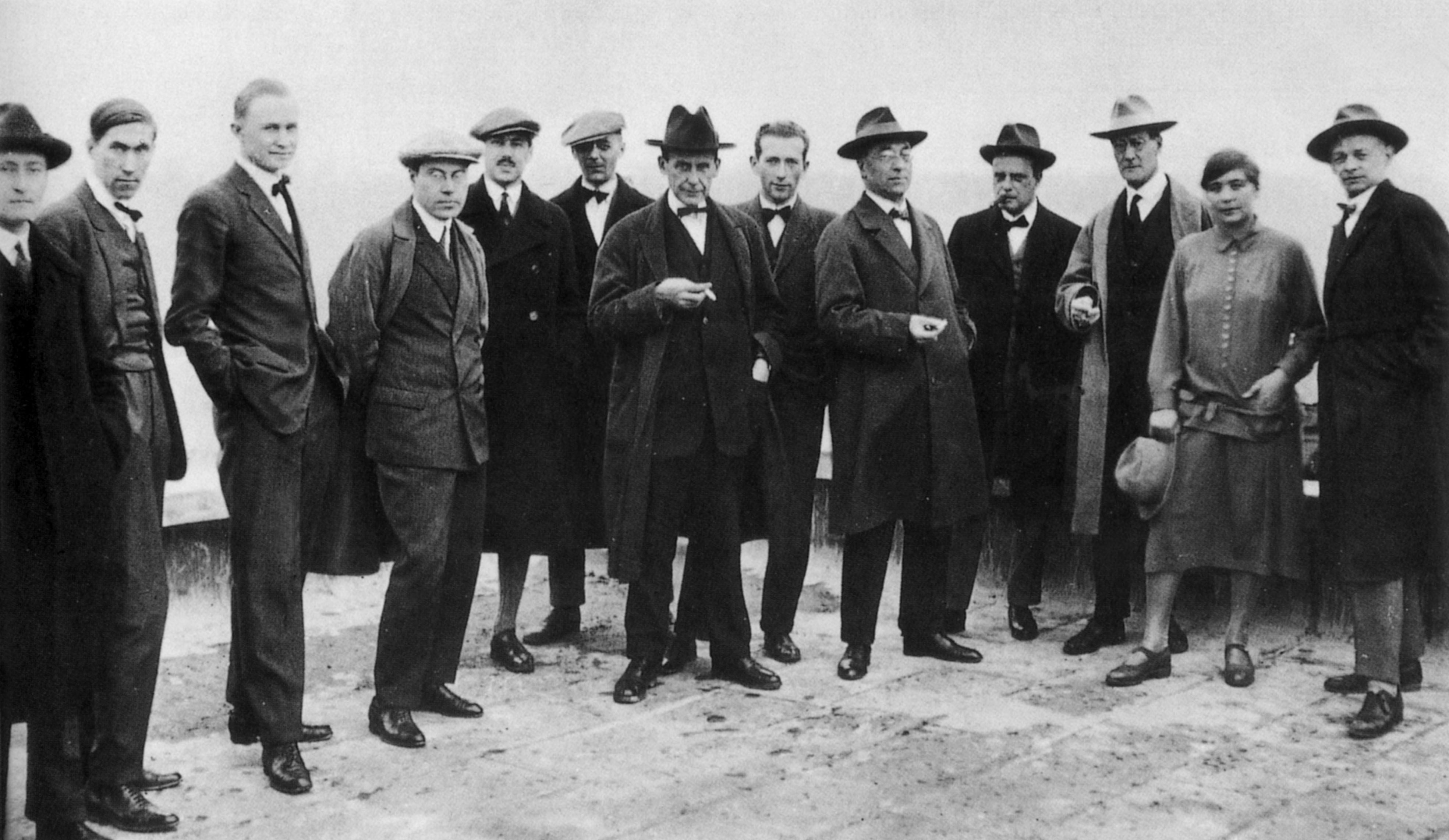 A group of men and one woman in early 20th-century attire pose together outdoors.