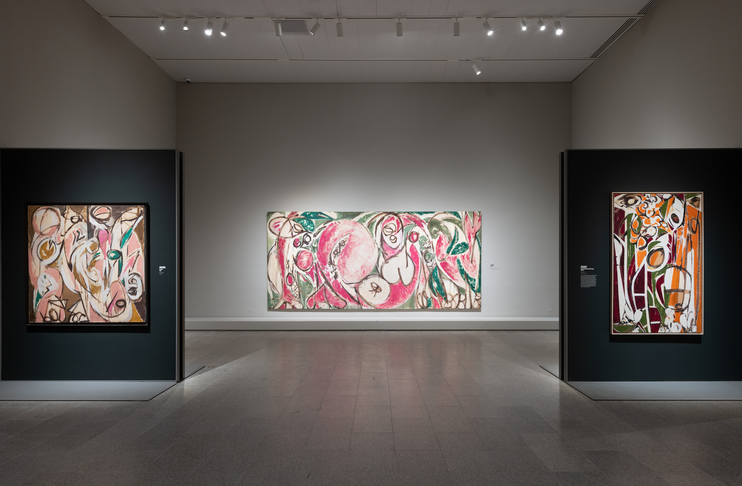 A modern art gallery displays three abstract paintings with swirling, colorful forms on neutral walls.