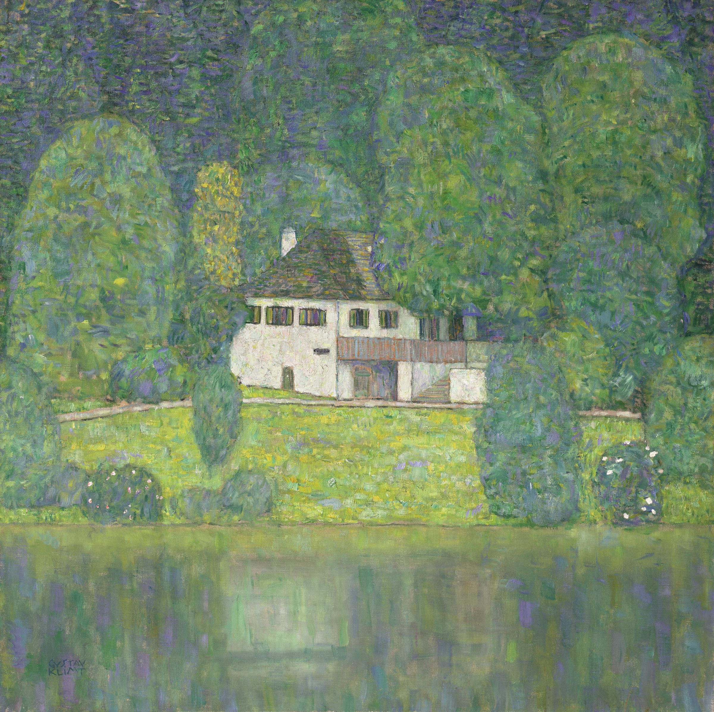 A white house sits by a lake, surrounded by lush green trees and reflected in the calm water.