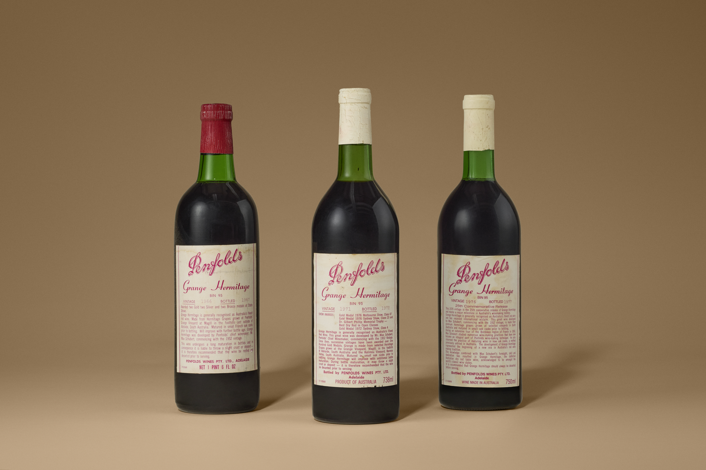 Three bottles of Penfolds Grange Hermitage red wine are displayed against a brown background.