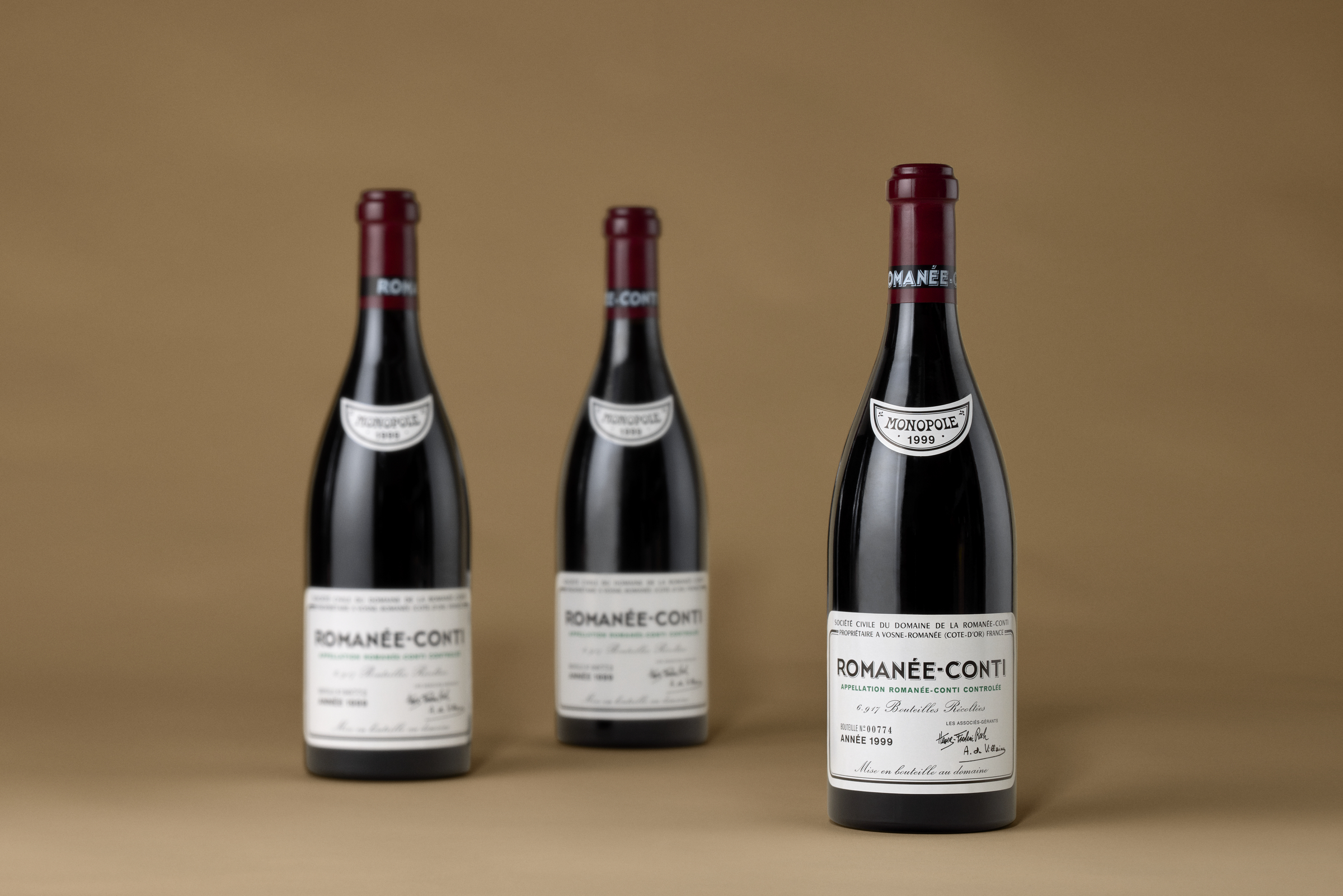 Three bottles of Romanée-Conti wine are displayed against a plain brown background.