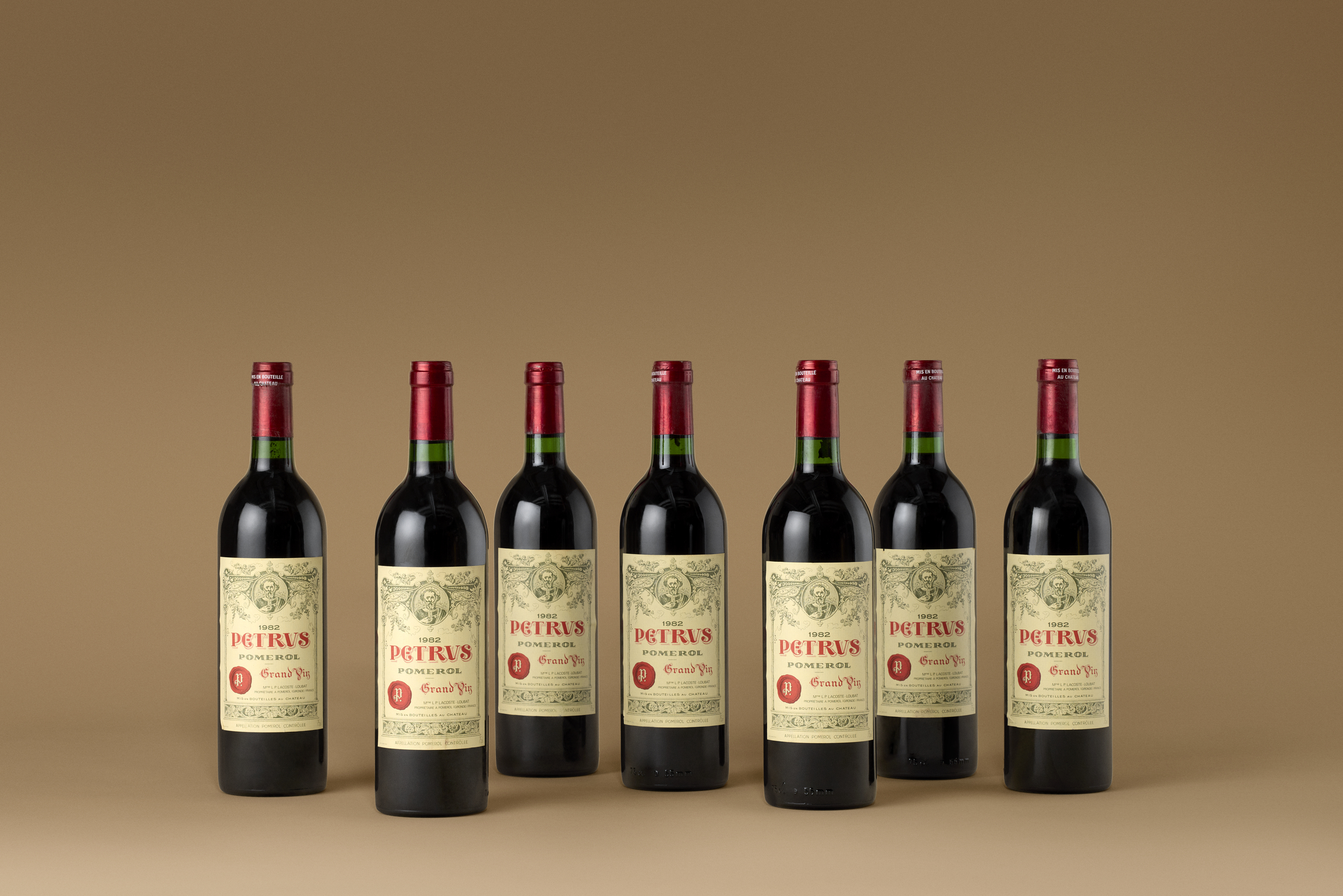 Six bottles of Petrus Pomerol red wine are arranged in a row against a brown background.