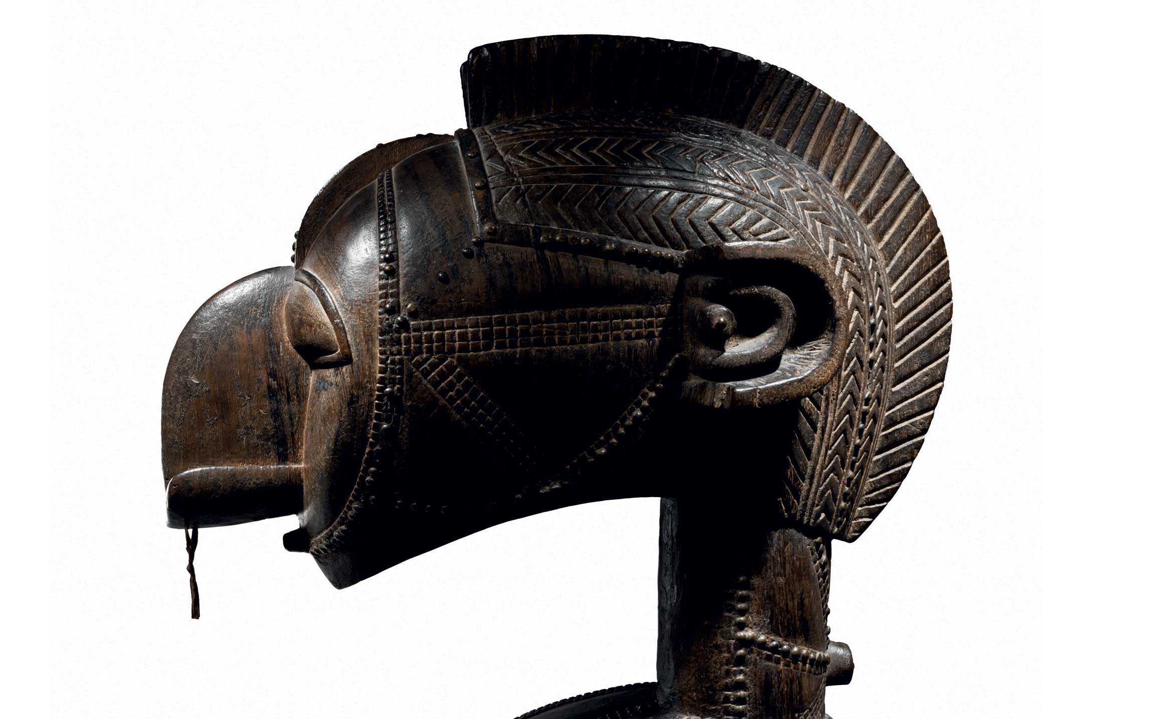 Side view of a carved wooden African mask with intricate patterns and a protruding cylindrical hairstyle.