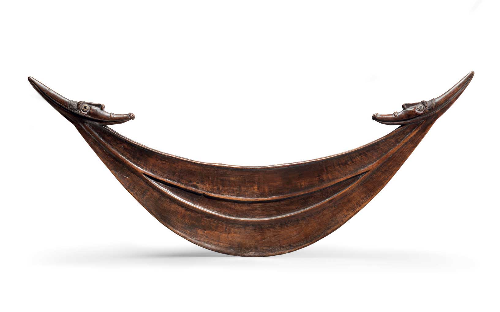 An antique wooden canoe with intricate, decorative heads at both ends, set against a plain white background.