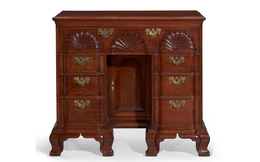 An elegant wooden antique cabinet with decorative shell carvings and brass handles.