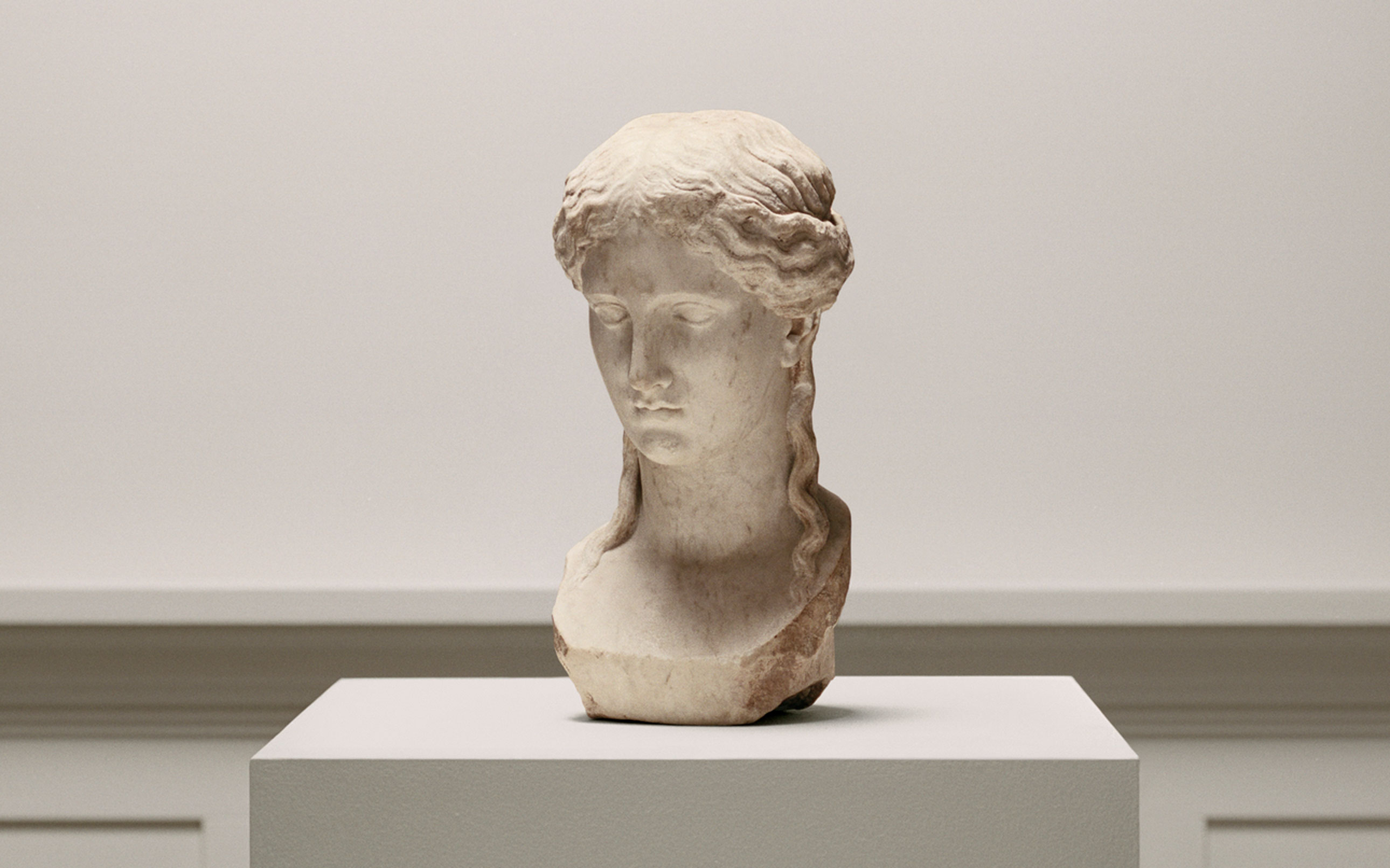 The image displays an ancient sculpture of a torso on a pedestal, notably deteriorated, set against a plain background.