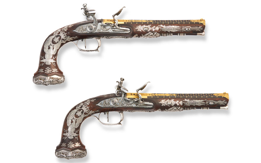Two ornately decorated antique flintlock pistols with intricate inlays and engravings on a white background.