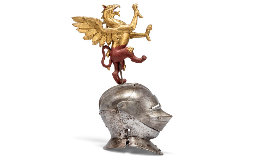 The image shows an ornate golden winged lion sculpture mounted on a weathered metal helmet.