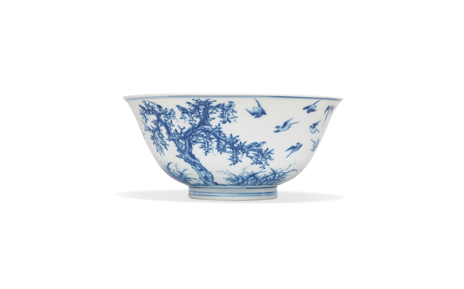 一个青花瓷碗，在素色背景上装饰着复杂的树木和鸟类图案。