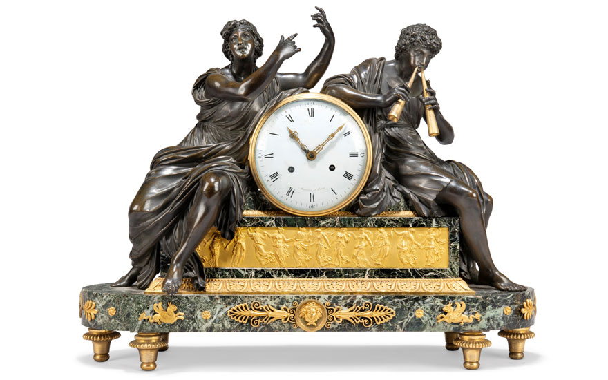 An ornate antique clock with a large round white dial flanked by two classical bronze figures on a decorative marble and golden base.
