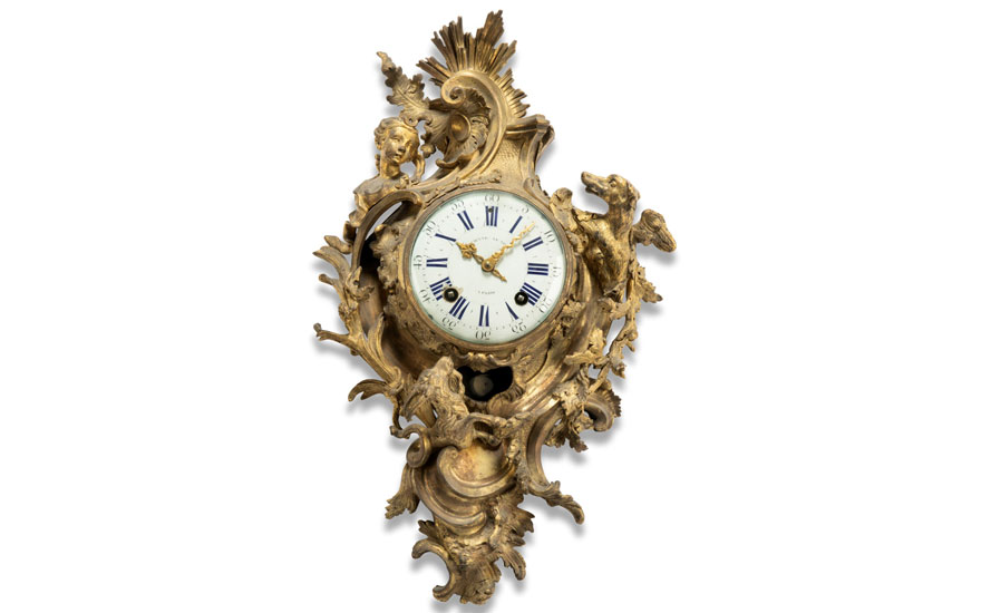Ornate golden wall clock with intricate designs including figures and foliage, featuring a white dial with Roman numerals.