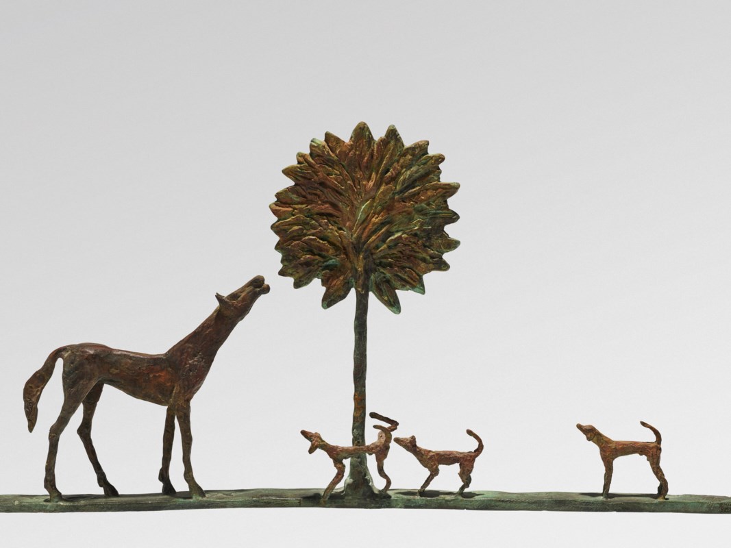 A sculpture depicting a dog and three smaller dogs in bronze, looking at a stylized tree.
