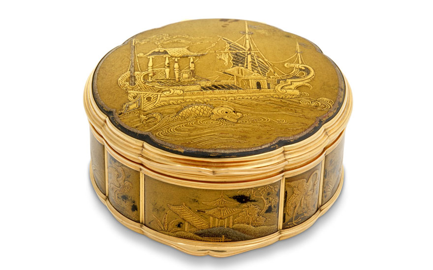 An ornate golden casket featuring intricate engravings of maritime scenes and Asian architecture.