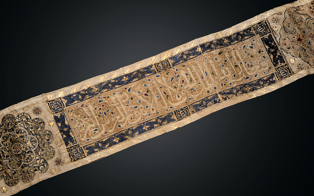 An ornate embroidered textile featuring intricate Islamic calligraphy and detailed, decorative patterns against a dark background.