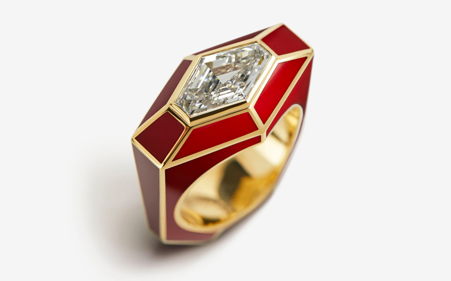 A gold ring with a large diamond set in a geometric red enamel frame on a white background.