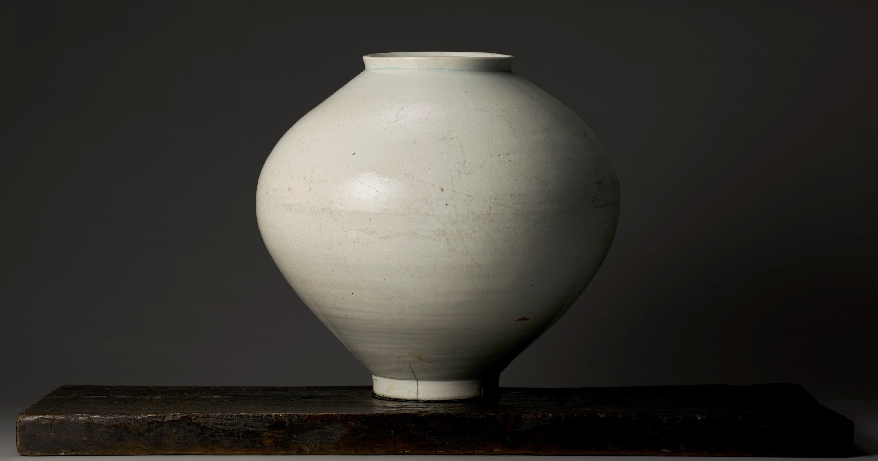 An elegant white ceramic vase stands on a dark wooden base against a muted background.