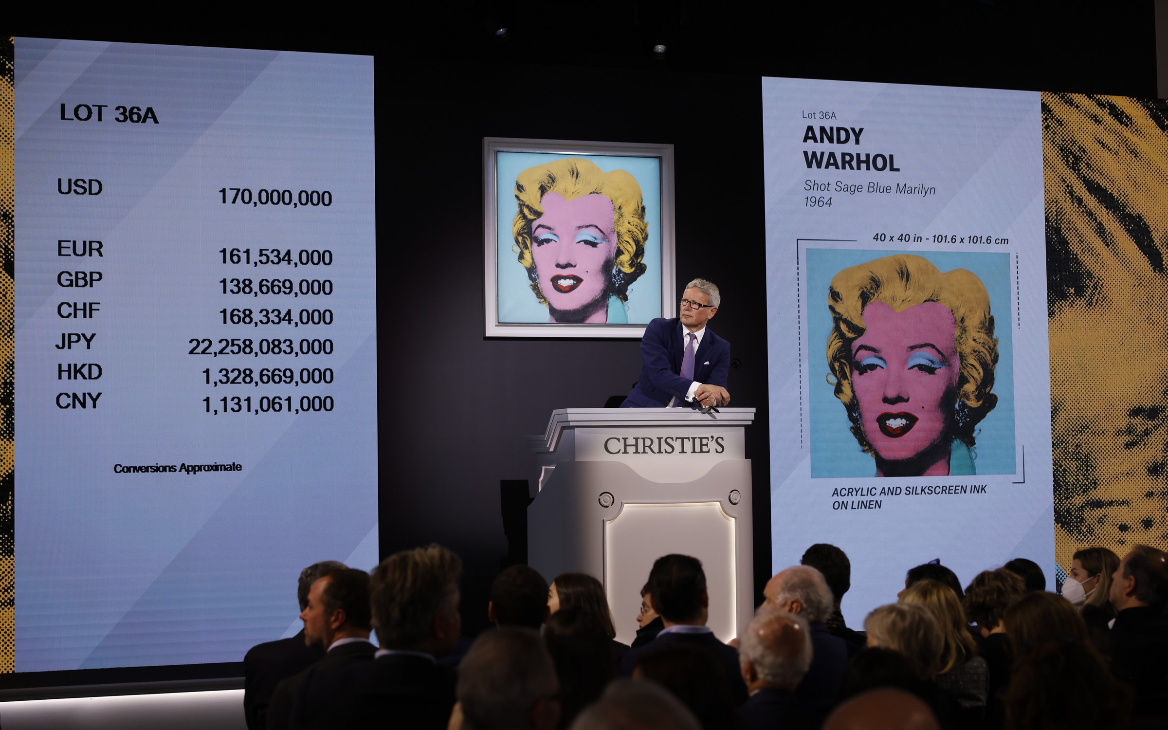 An auction at Christie's featuring Andy Warhol's "Shot Sage Blue Marilyn" with price conversions displayed on a large screen.