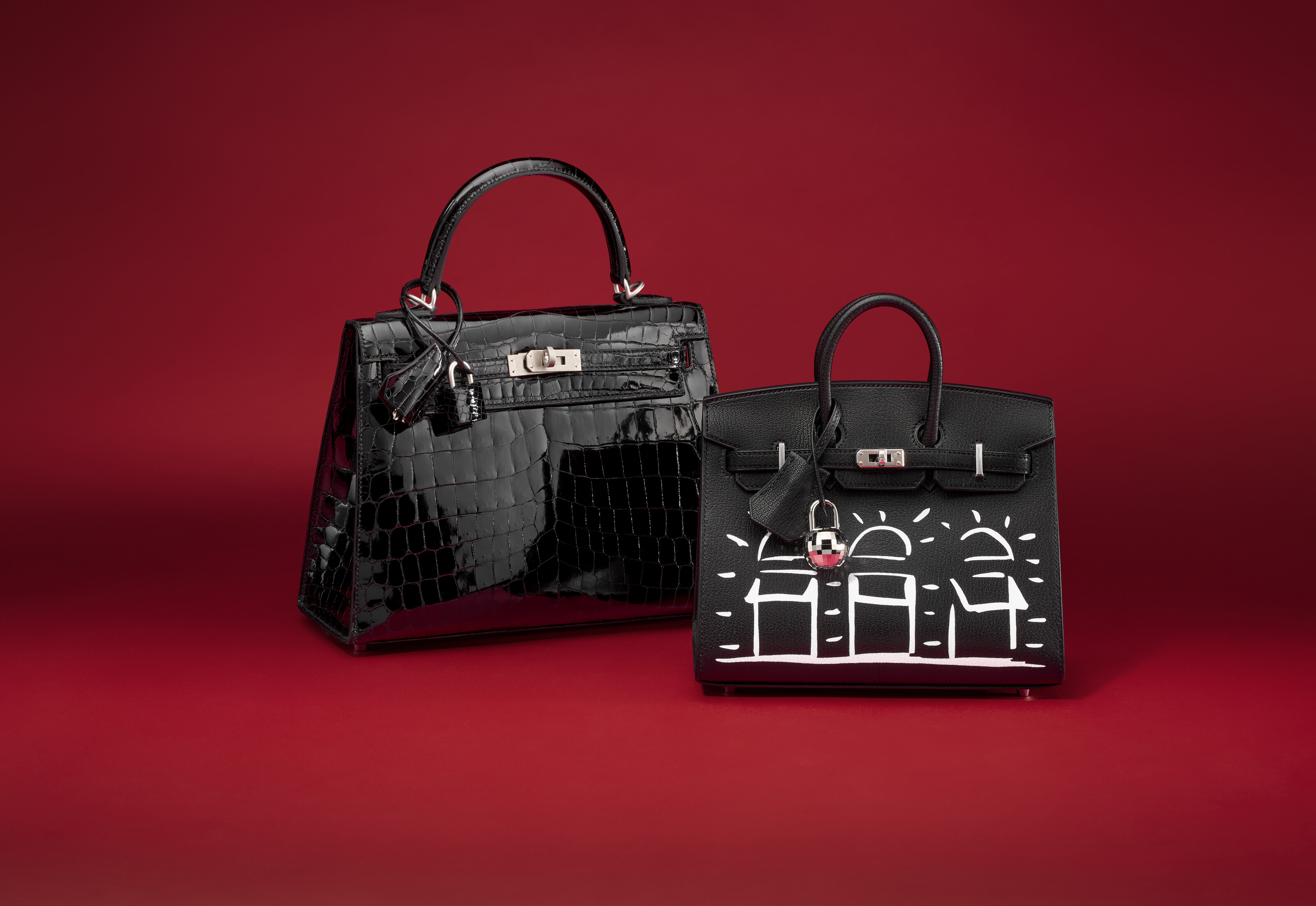 Two black handbags are displayed on a red background, one with white artistic designs.