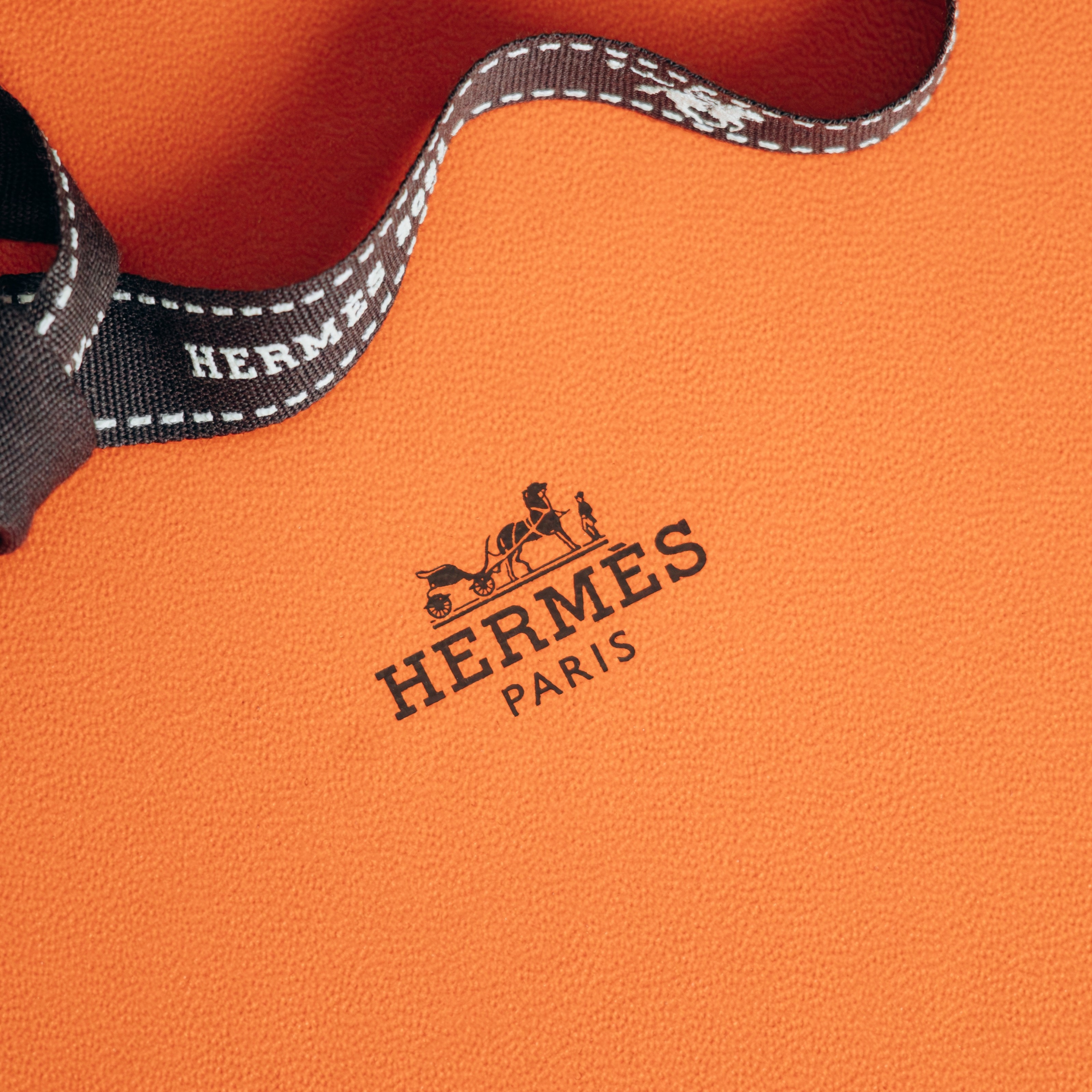 An orange Hermes Paris box with a brown ribbon featuring the Hermes logo and design.