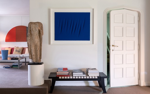 A modern interior features abstract art, a sculpture, books, and an open white door.