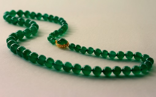 A green beaded necklace with a gold clasp is displayed on a light surface.