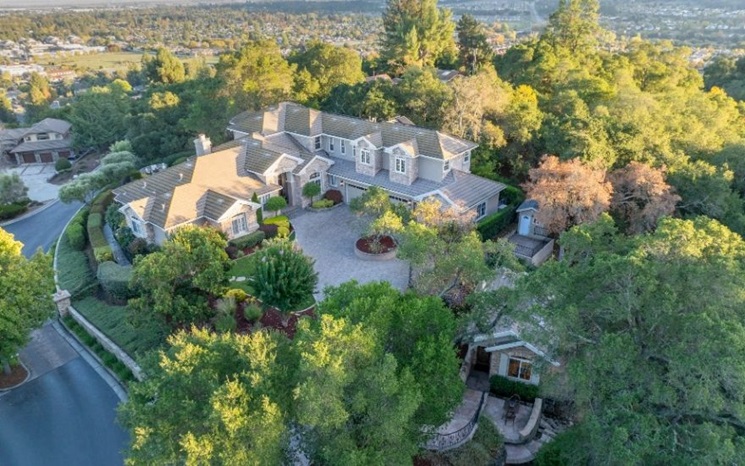 A large, elegant house is surrounded by lush greenery and trees, located in a quiet, upscale neighborhood.