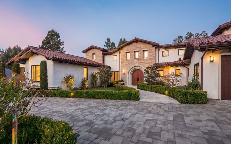 A large Mediterranean-style house with red tile roof, stone entry, and landscaped driveway.