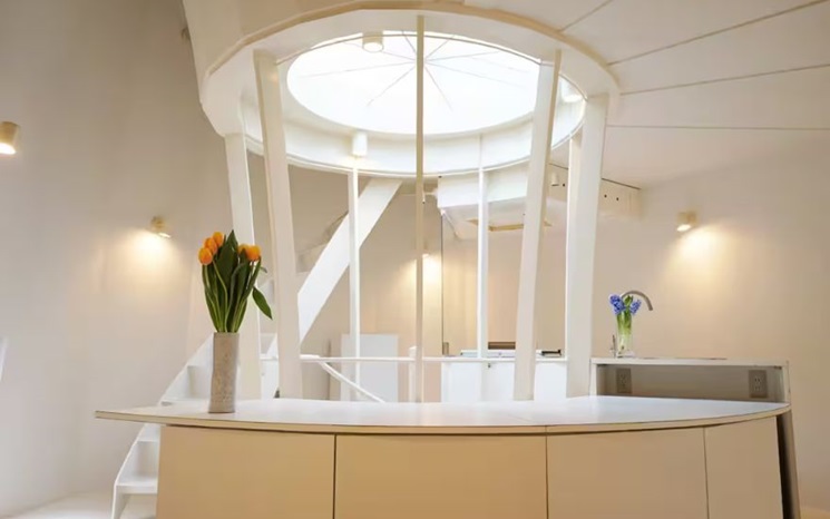 Modern white room with curved architecture, skylight, and vases of flowers on the counter.