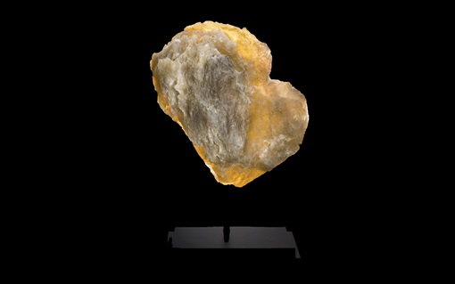 A rough, yellowish-brown mineral or rock specimen is displayed against a black background.