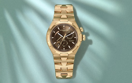 A gold-toned wristwatch with a brown dial lies on a textured blue surface, casting a shadow.
