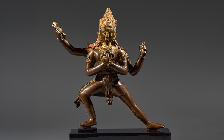 A bronze statue of a deity with four arms, adorned with a crown and intricate jewelry.