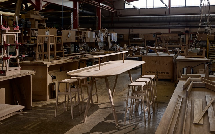 A woodworking shop with wooden tables, stools, tools, and various projects in progress.