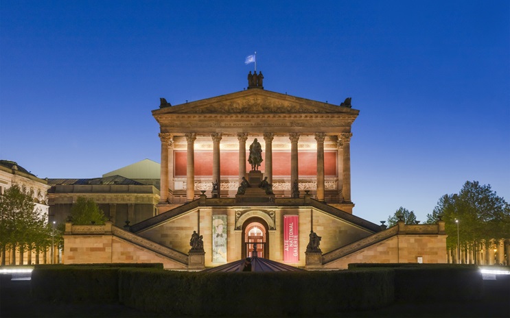 A grand neoclassical building with columns is lit up against a clear evening sky.