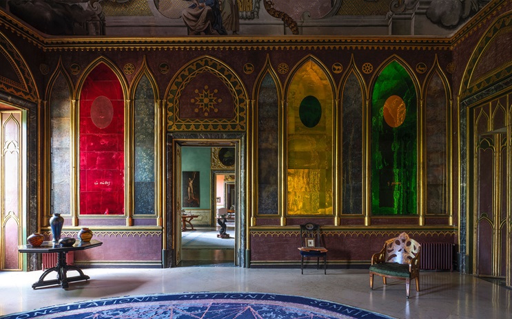 A richly decorated room features colorful stained glass panels, ornate gold accents, and elegant furniture.