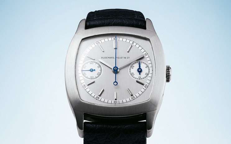 A luxury silver wristwatch with a square case and two subdials on a black leather strap.