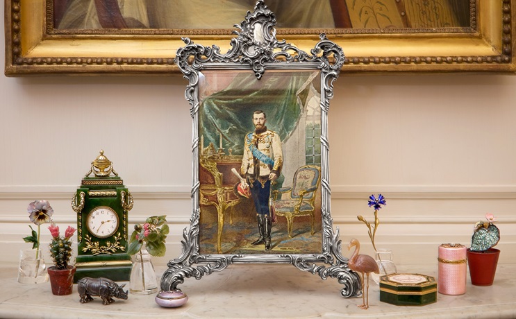 A decorative framed portrait of a royal figure is displayed among ornate objects and flowers.