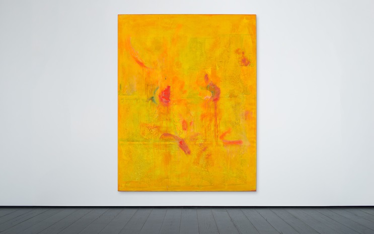A large abstract painting with dominant yellow and orange hues and some red and pink accents.