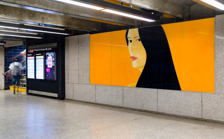 A large portrait artwork of a woman with black hair is displayed on a yellow wall in a subway station.